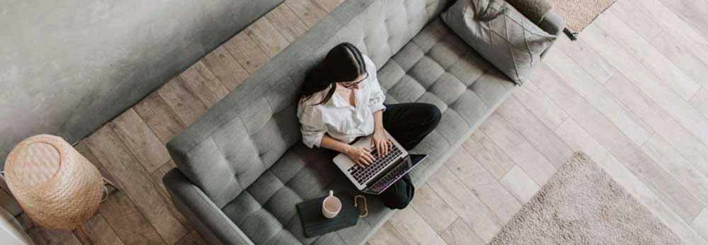 Employee working from home on her couch, enjoying a cup of coffee