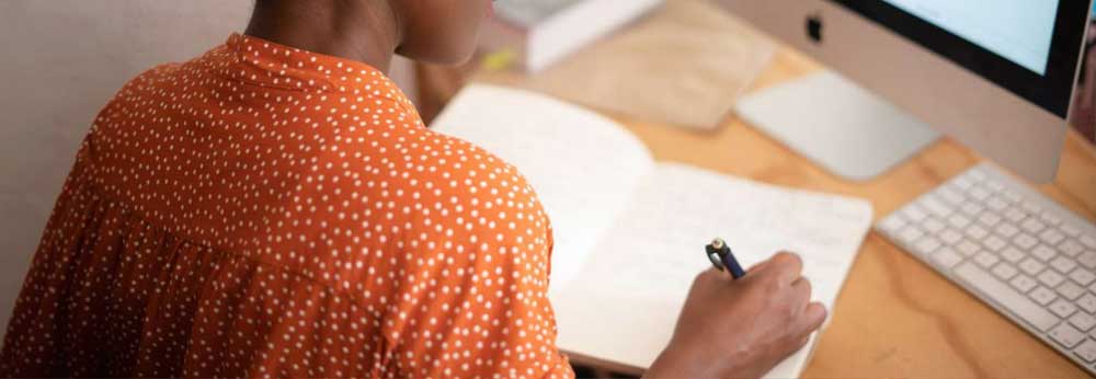 Woman writing down notes in from of her workspace